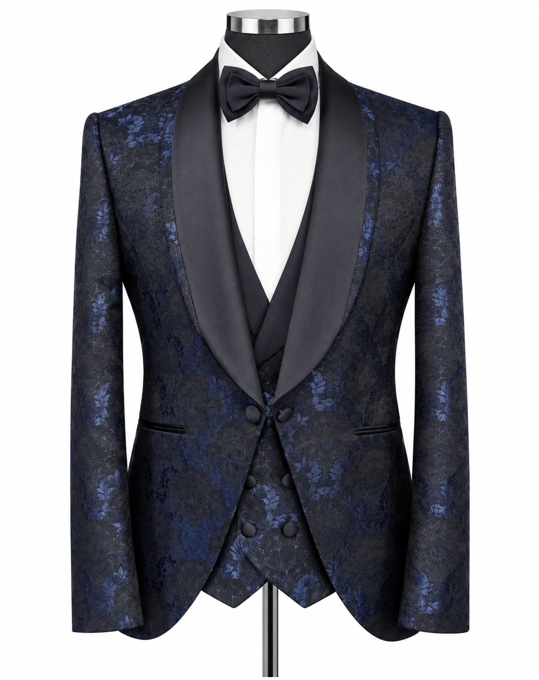 A men's formal tuxedo jacket and vest set on a mannequin, featuring a dark blue and black brocade patterned fabric with contrasting black satin shawl lapels, styled with a white dress shirt and black bow tie.