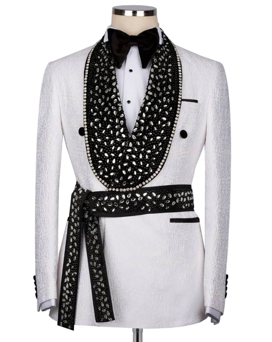 A white textured tuxedo jacket displayed on a mannequin with a black bow tie, white dress shirt, and a large black embellished shawl with a matching patterned waist tie.