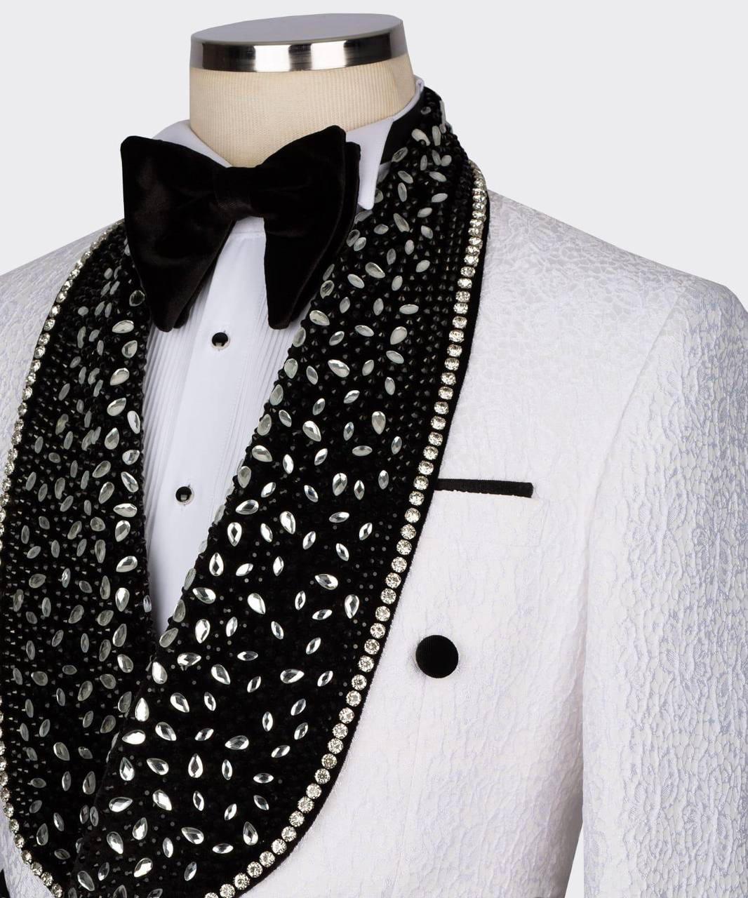 A close-up of a white textured tuxedo jacket on a mannequin torso, styled with a black velvet bow tie and a wide black beaded scarf embellished with silver rhinestones.
