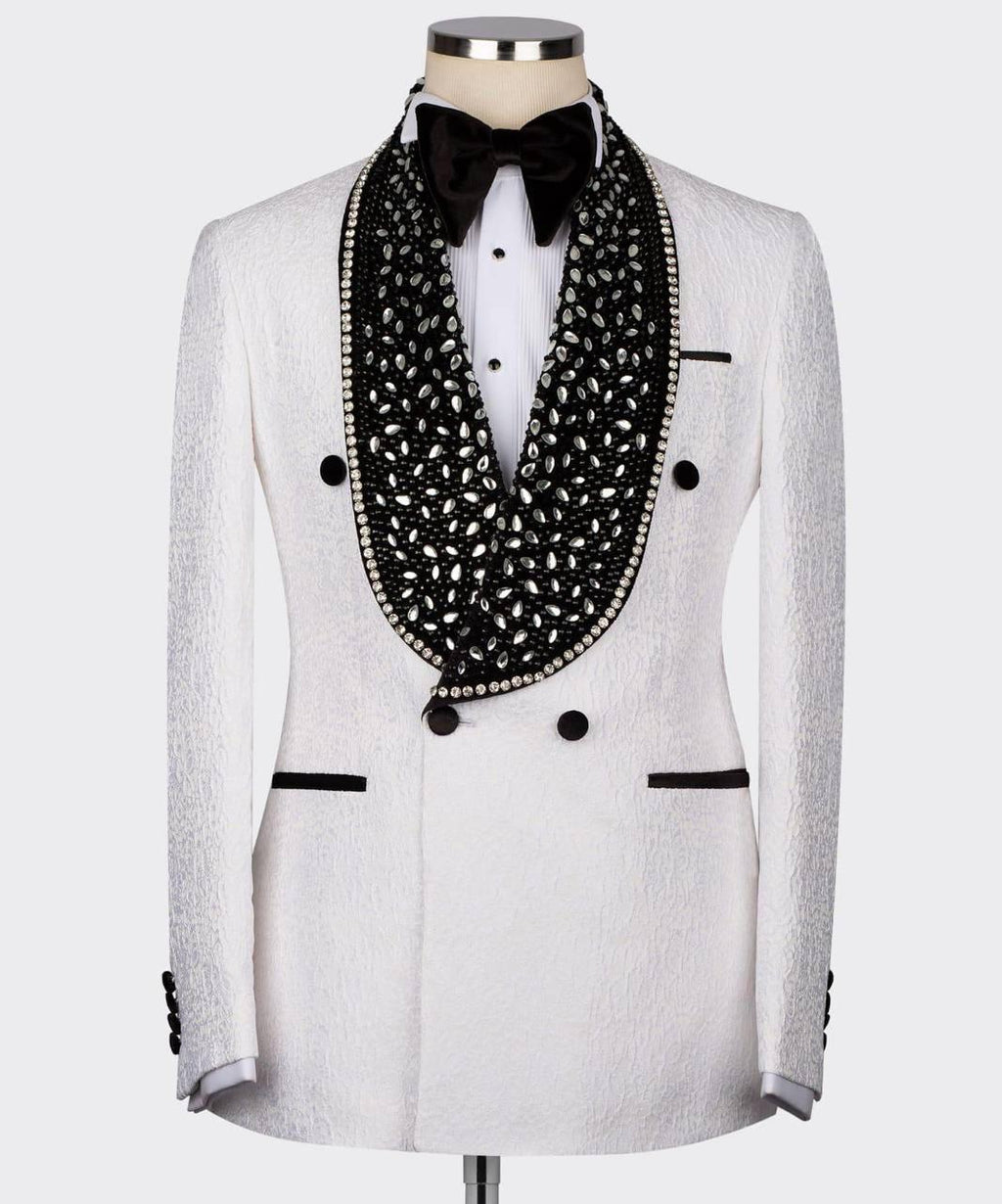 A white textured double-breasted tuxedo jacket displayed on a mannequin with a white shirt, black bow tie, and a prominent black beaded collar with silver rhinestone trim.