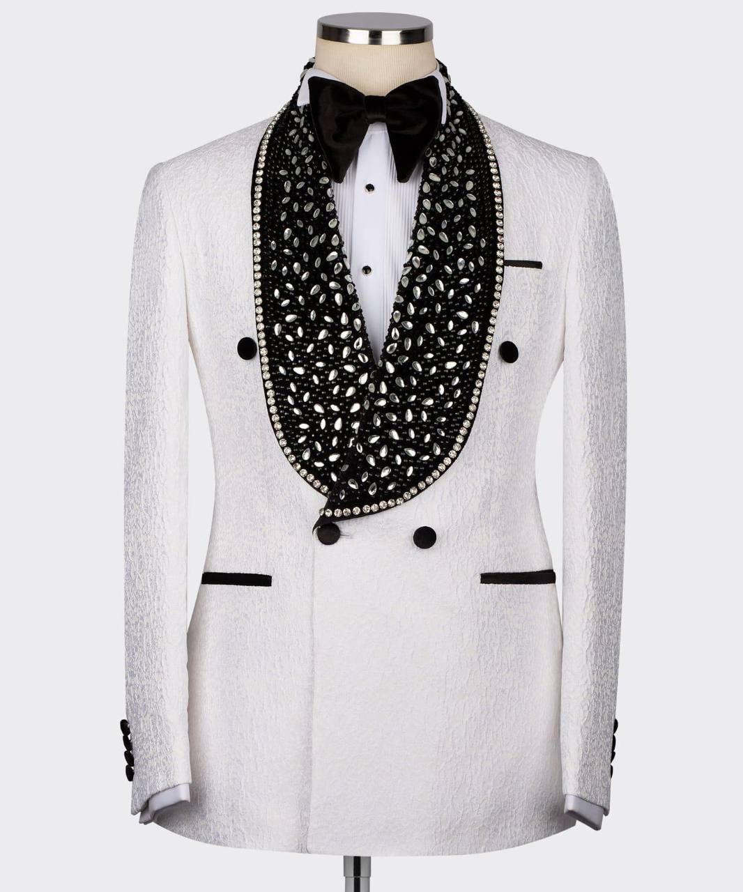 A white textured double-breasted tuxedo jacket displayed on a mannequin with a white shirt, black bow tie, and a prominent black beaded collar with silver rhinestone trim.