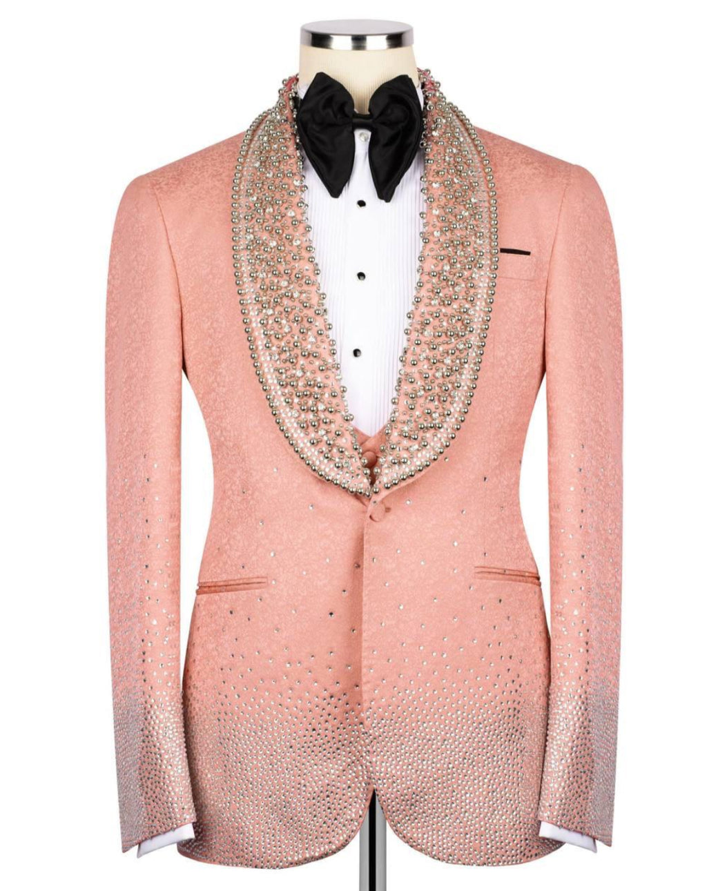 A peach-colored tuxedo jacket embellished with sparkling rhinestones, styled on a mannequin with a white pleated shirt, black bow tie, and a matching rhinestone-trimmed collar.