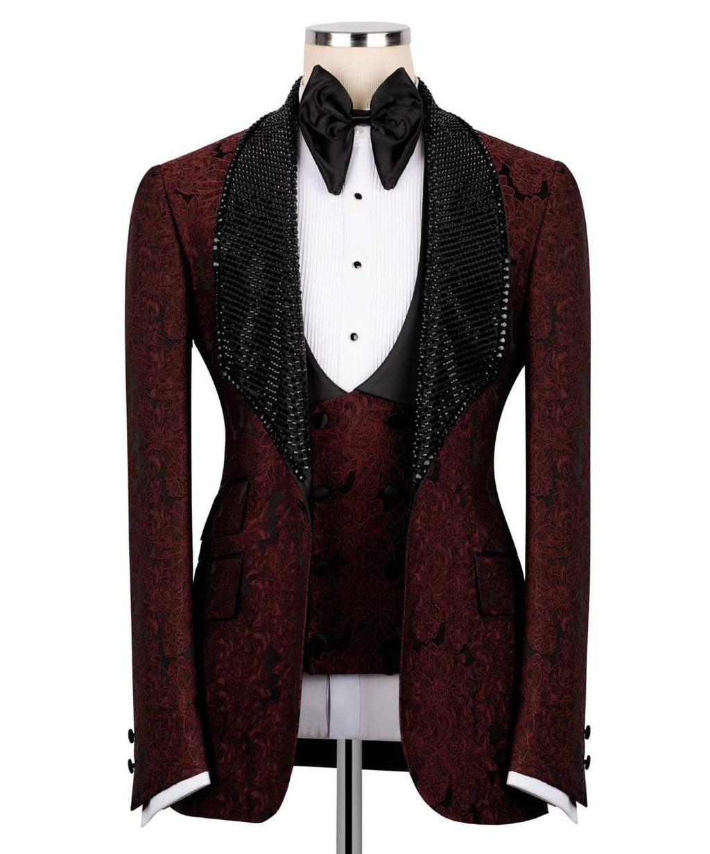 A men's tuxedo jacket with a dark burgundy and black damask pattern, featuring wide black beaded shawl lapels, styled on a mannequin with a white pleated shirt, black bow tie, and matching waistcoat.