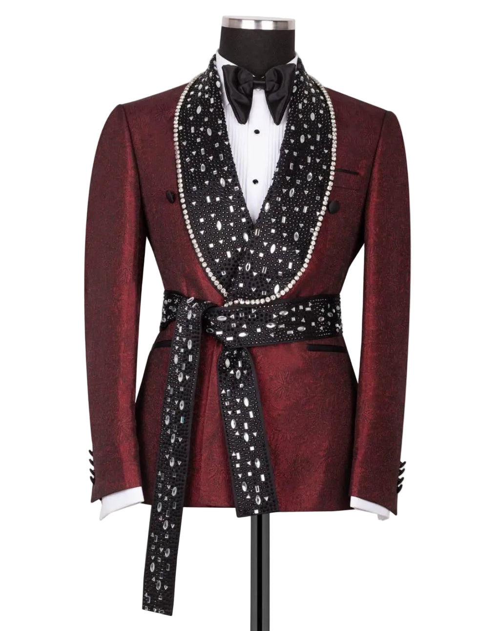 A men's tuxedo jacket displayed on a mannequin against a light gray background. The jacket is a deep burgundy with a subtle brocade pattern, featuring a black shawl collar embellished with white pearls, a matching black waist tie with white polka dots, a white dress shirt, and a black bow tie.