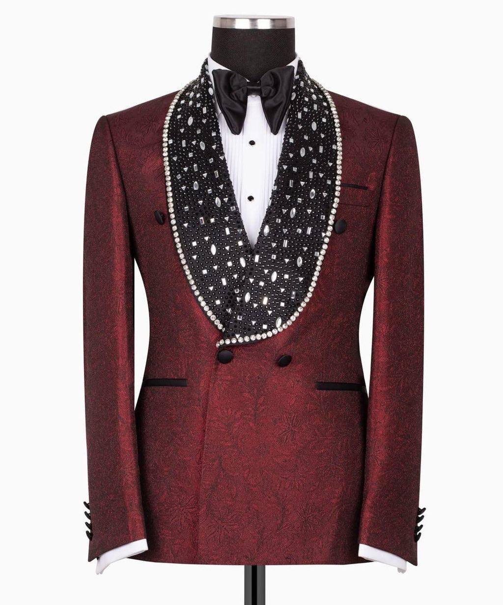 A men's tuxedo jacket displayed on a mannequin, featuring a deep burgundy brocade pattern with a wide black shawl collar heavily embellished with white pearls and silver rhinestones, styled with a white dress shirt and black bow tie.