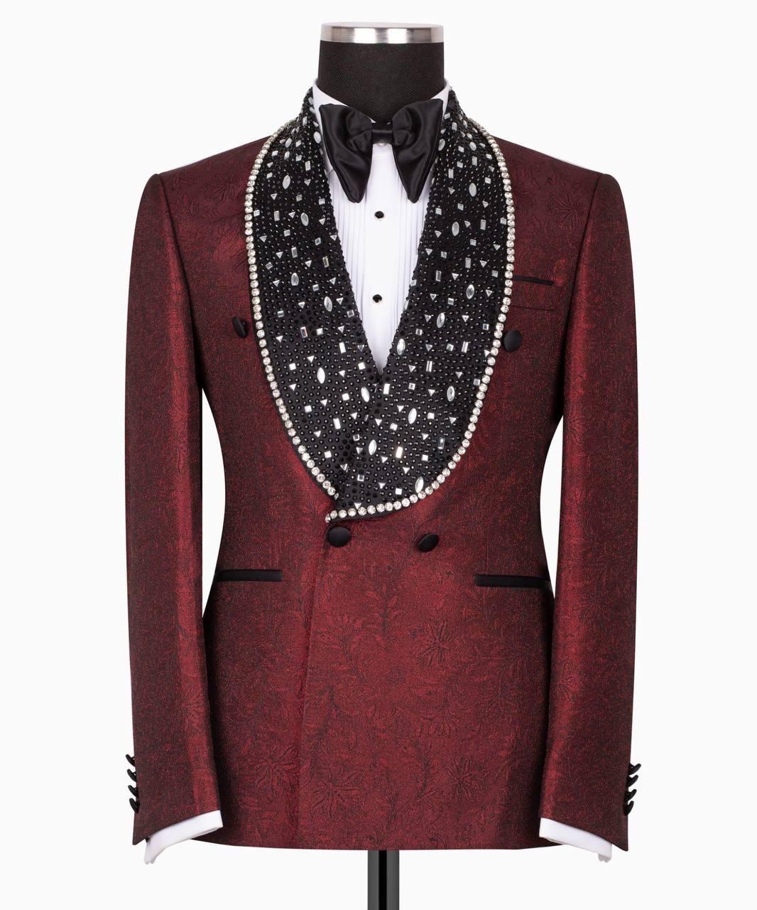 A men's tuxedo jacket displayed on a mannequin, featuring a deep burgundy brocade pattern with a wide black shawl collar heavily embellished with white pearls and silver rhinestones, styled with a white dress shirt and black bow tie.