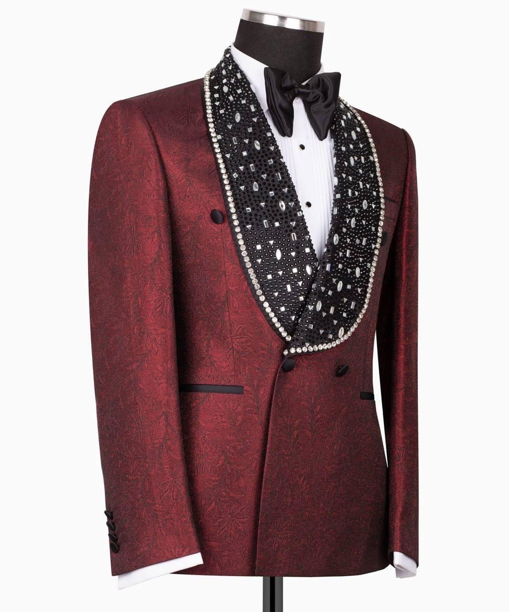 A men's tuxedo jacket displayed on a mannequin, featuring a deep burgundy brocade pattern, a wide black shawl lapel embellished with white pearls, a white dress shirt, and a black bow tie.