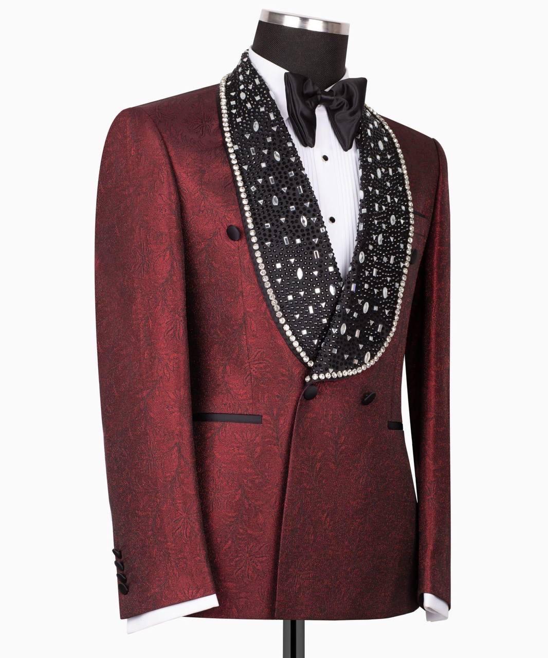 A men's tuxedo jacket displayed on a mannequin, featuring a deep burgundy brocade pattern, a wide black shawl lapel embellished with white pearls, a white dress shirt, and a black bow tie.
