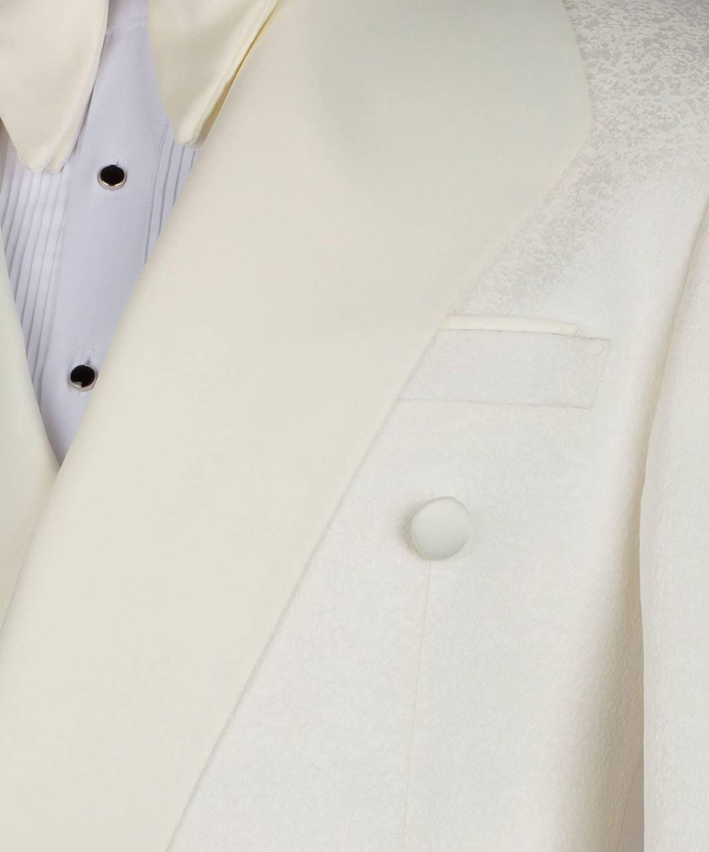 Close-up of a cream-colored double-breasted tuxedo jacket with satin lapels, a textured patterned lining on the shoulder, and a white dress shirt with black buttons.