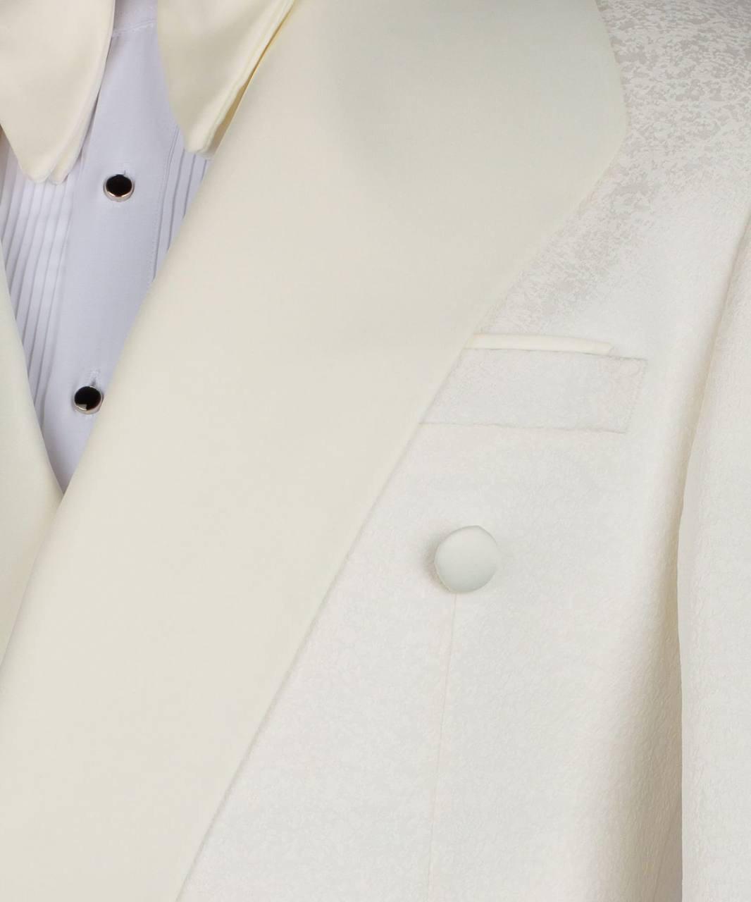 Close-up of a cream-colored double-breasted tuxedo jacket with satin lapels, a textured patterned lining on the shoulder, and a white dress shirt with black buttons.