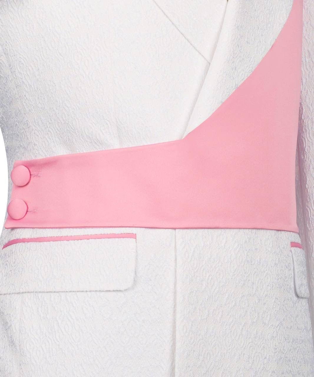 A close-up of a white textured blazer featuring a contrasting pink diagonal sash detail across the chest with two decorative buttons on the left side.