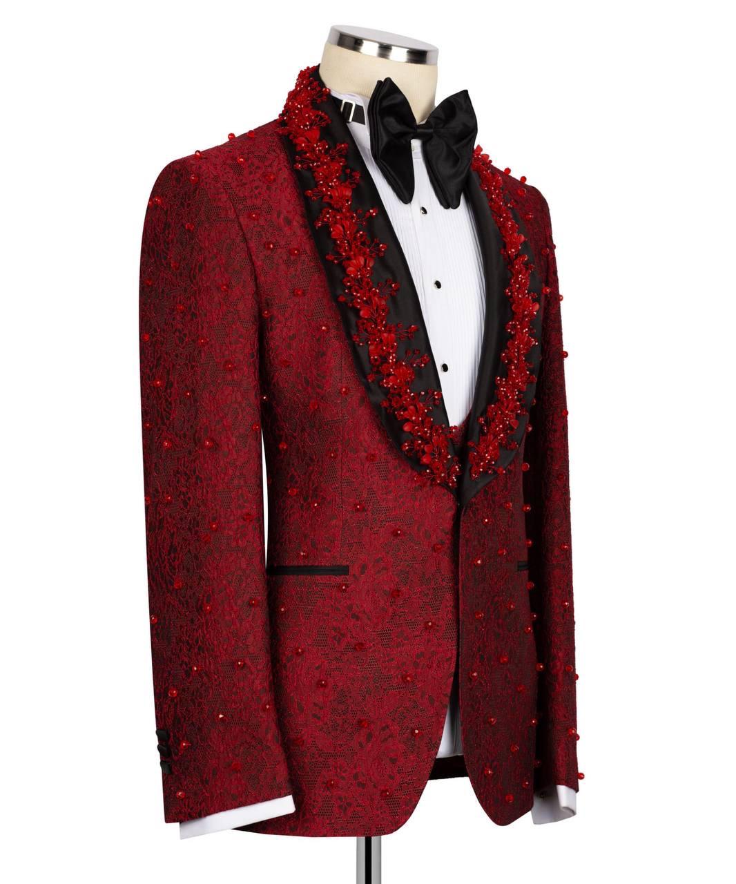 A red patterned tuxedo jacket with black satin peak lapels, embellished with red floral embroidery and bead details, styled on a mannequin with a white shirt and black bow tie.
