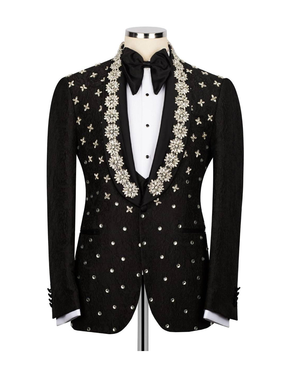 A black tuxedo jacket with ornate silver and gold star-patterned beadwork and embroidery, styled on a mannequin with a white shirt, black bow tie, and white cufflinks.