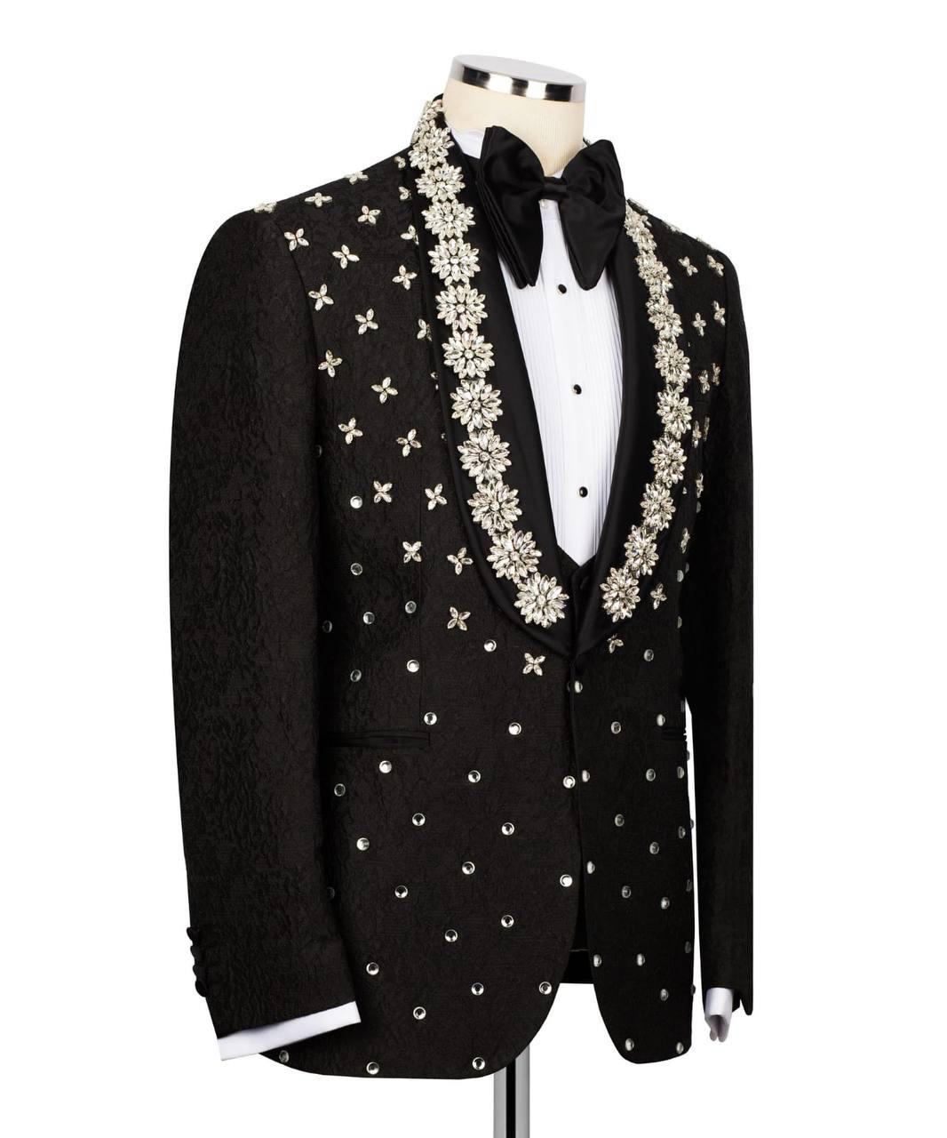 A black tuxedo jacket with ornate silver and white beaded floral patterns on the lapels and shoulders, displayed on a mannequin with a white dress shirt and black bow tie against a white background.