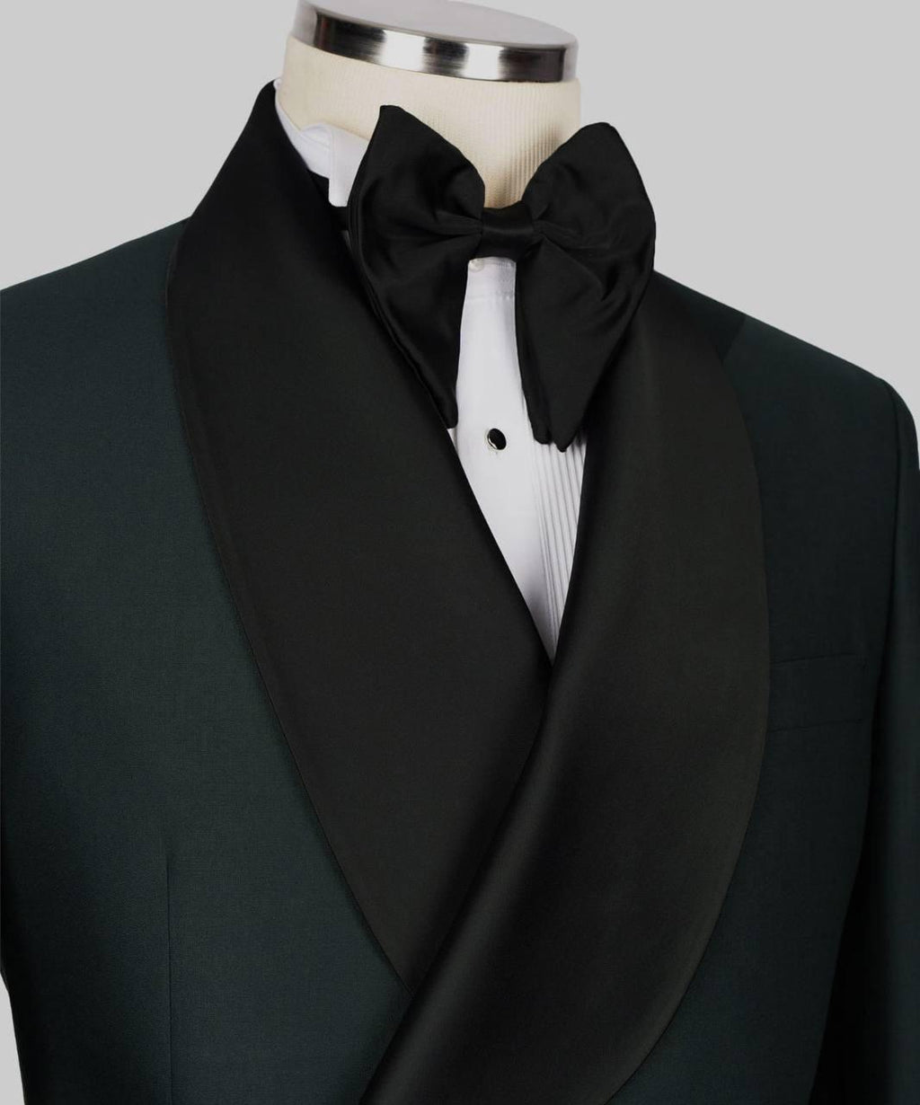 A close-up of a formal tuxedo jacket on a mannequin, featuring a black shawl collar, a black bow tie, and a white pleated dress shirt against a light gray background.