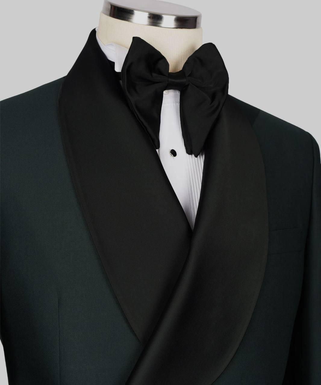 A close-up of a formal tuxedo jacket on a mannequin, featuring a black shawl collar, a black bow tie, and a white pleated dress shirt against a light gray background.