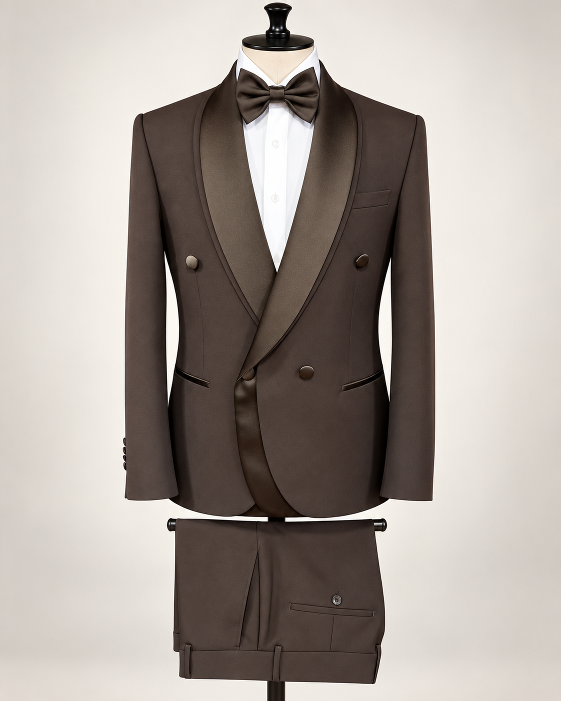 A dark brown double-breasted tuxedo jacket with satin shawl lapels, displayed on a mannequin with a matching bow tie and trousers, against a light beige background.