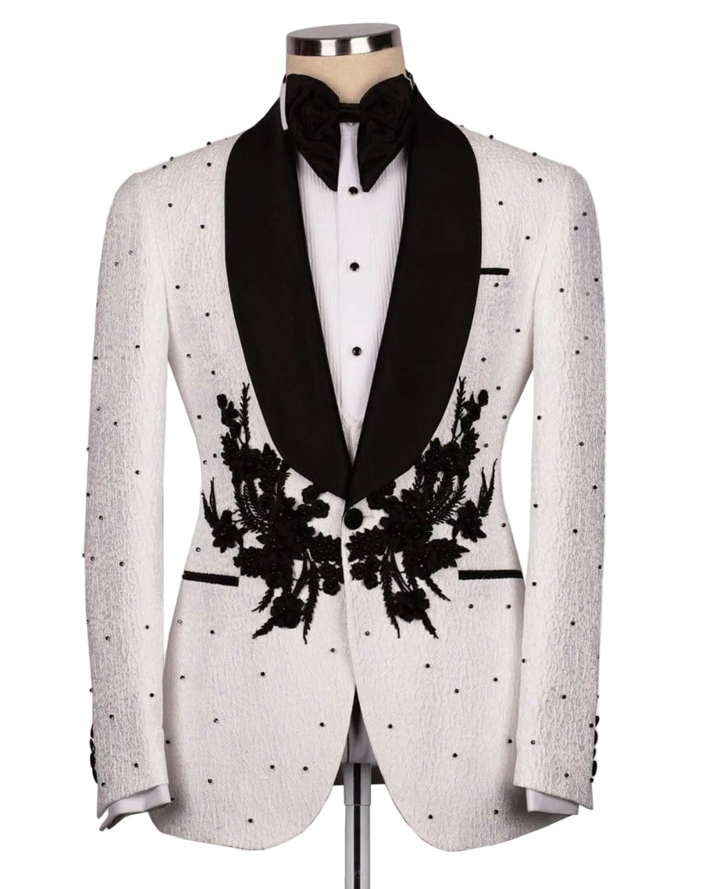 A white textured tuxedo jacket with black satin shawl collar, black floral embroidery on the front, and black polka dots, styled on a mannequin with a black bow tie and white shirt.