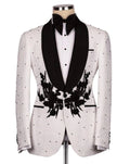 A white textured tuxedo jacket with black satin shawl collar, black floral embroidery on the front, and black polka dots, styled on a mannequin with a black bow tie and white shirt.