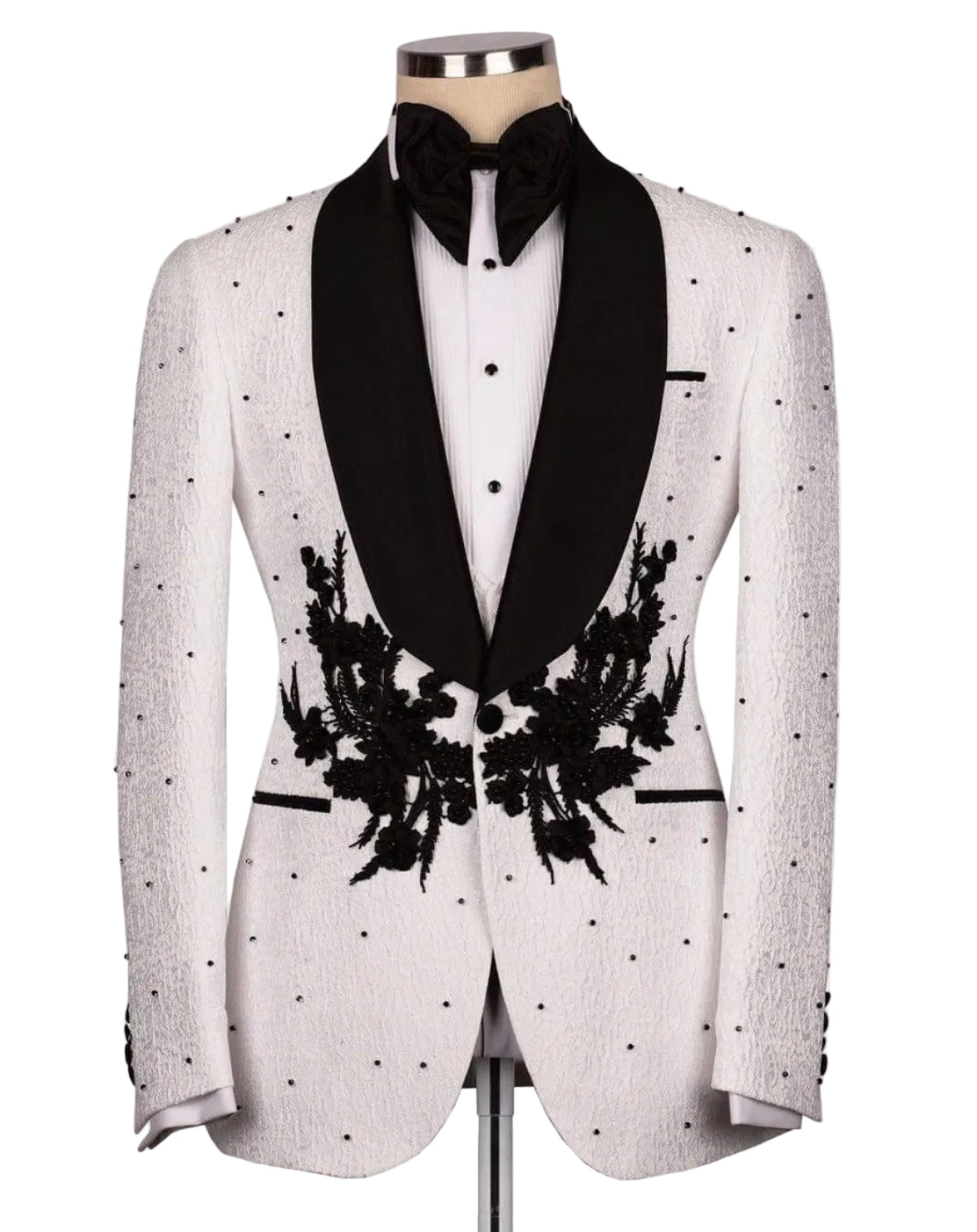 A white textured tuxedo jacket with black satin shawl collar, black floral embroidery on the front, and black polka dots, styled on a mannequin with a black bow tie and white shirt.