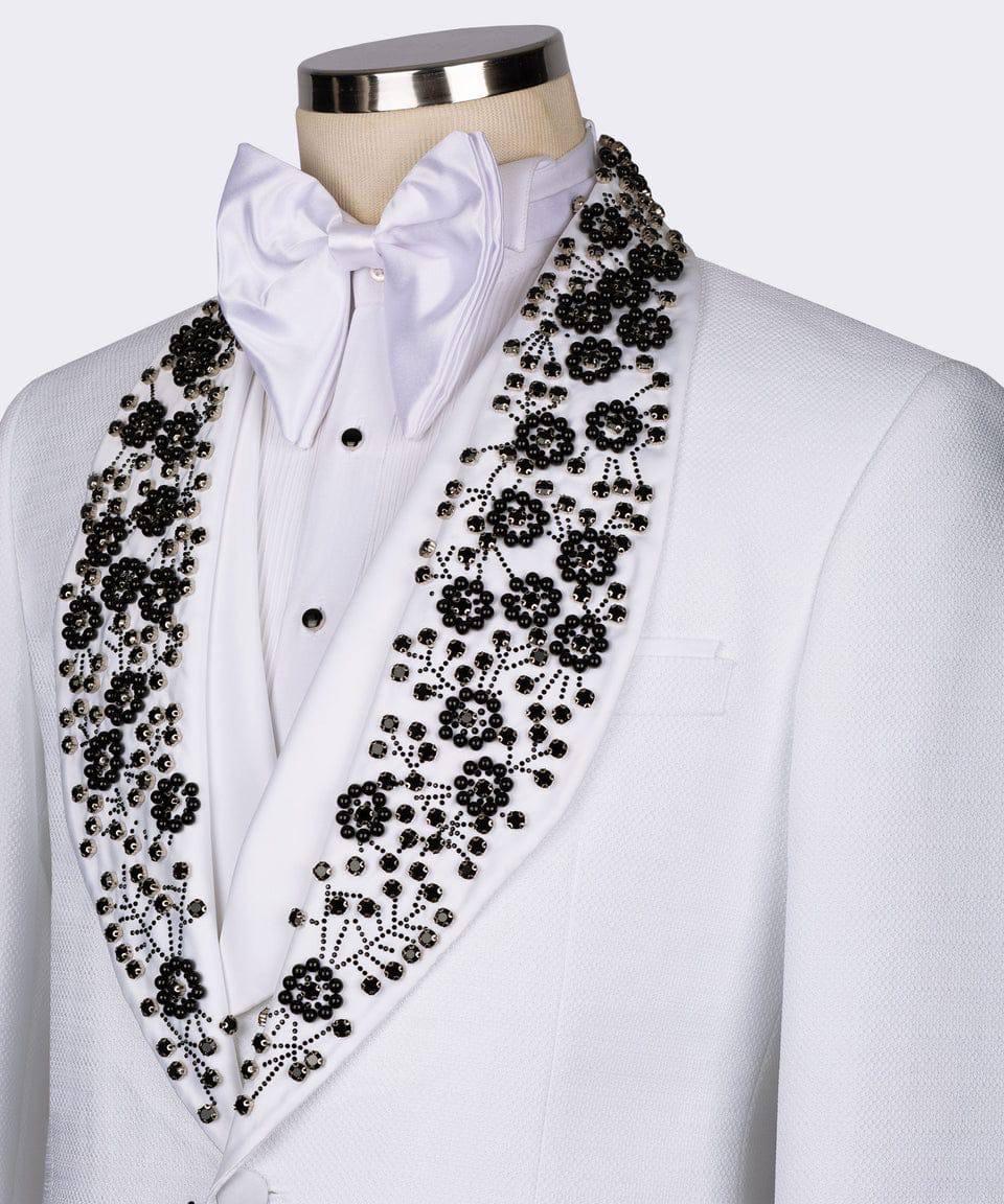 White formal tuxedo jacket with a white satin bow tie and white shirt, featuring dramatic black beaded floral embroidery along the shawl collar on a mannequin torso.