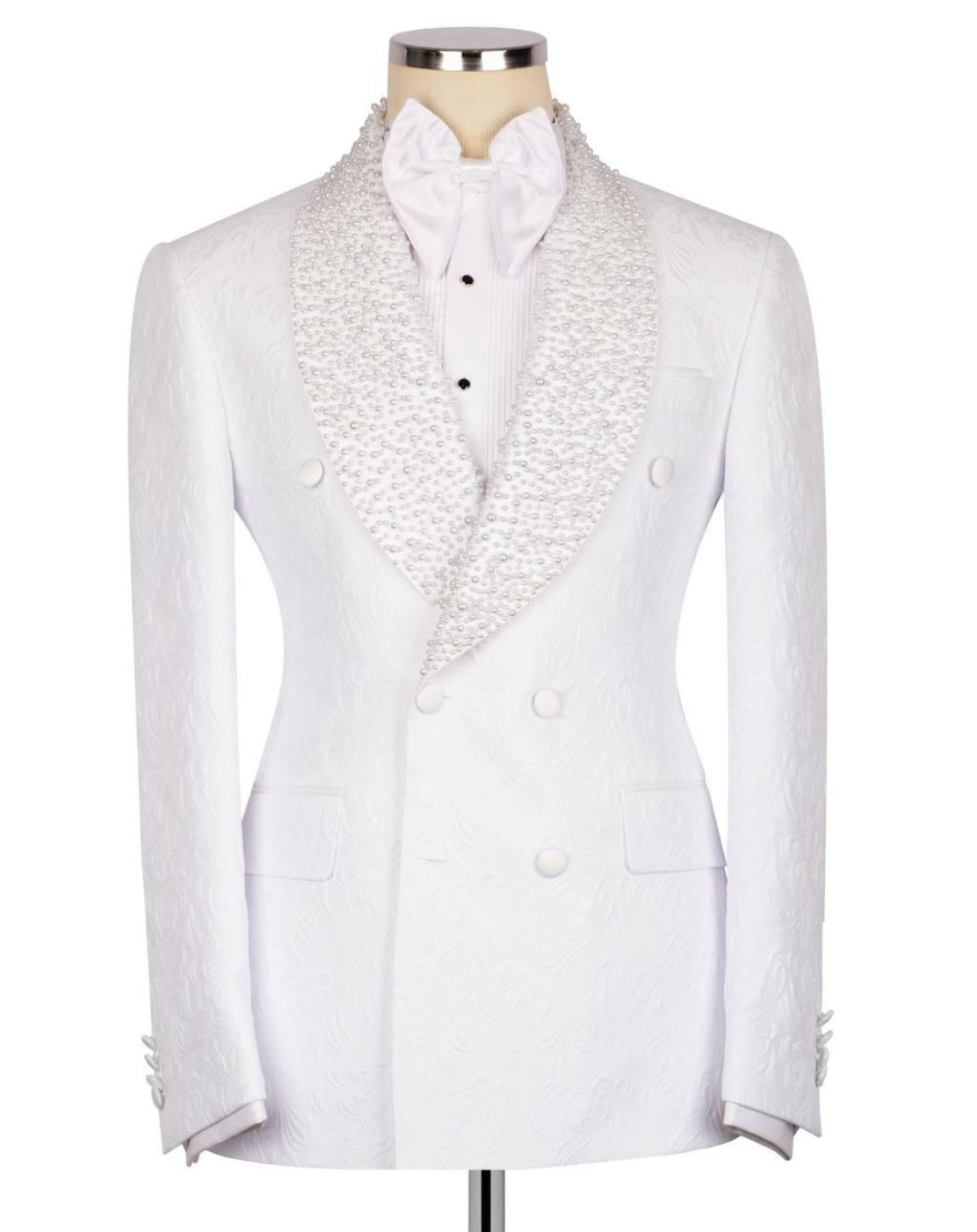 A white double-breasted tuxedo jacket with textured, patterned shawl lapels, displayed on a mannequin with a white bow tie and white dress shirt.