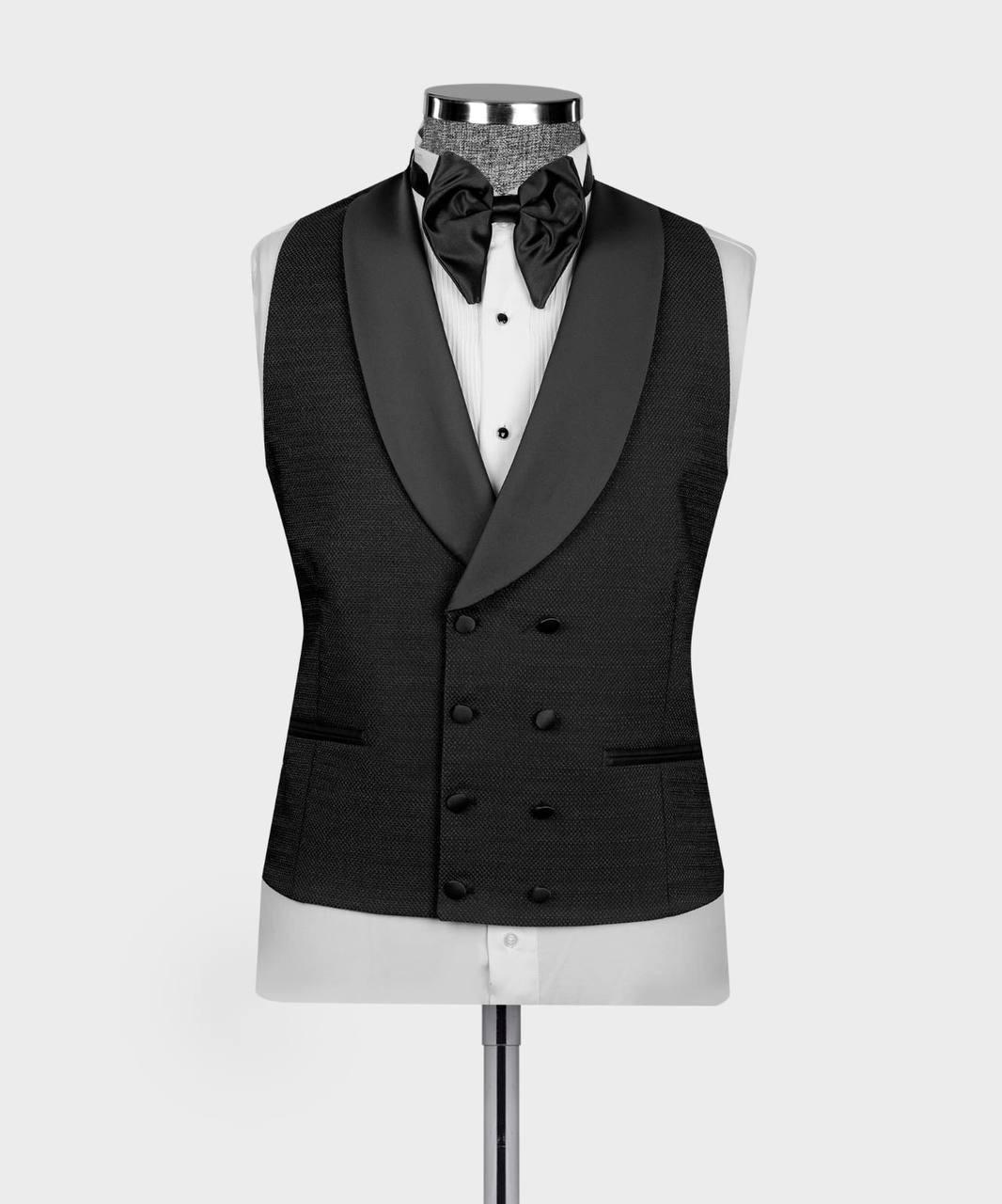 A black double-breasted tuxedo vest with satin peak lapels, displayed on a white dress shirt mannequin torso with a black bow tie and patterned neck scarf against a light gray background.