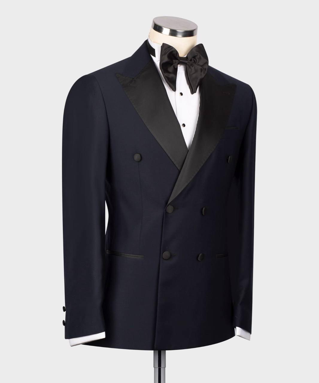 A navy blue double-breasted tuxedo jacket with black satin peak lapels, displayed on a mannequin torso with a black bow tie and white dress shirt against a light gray background.
