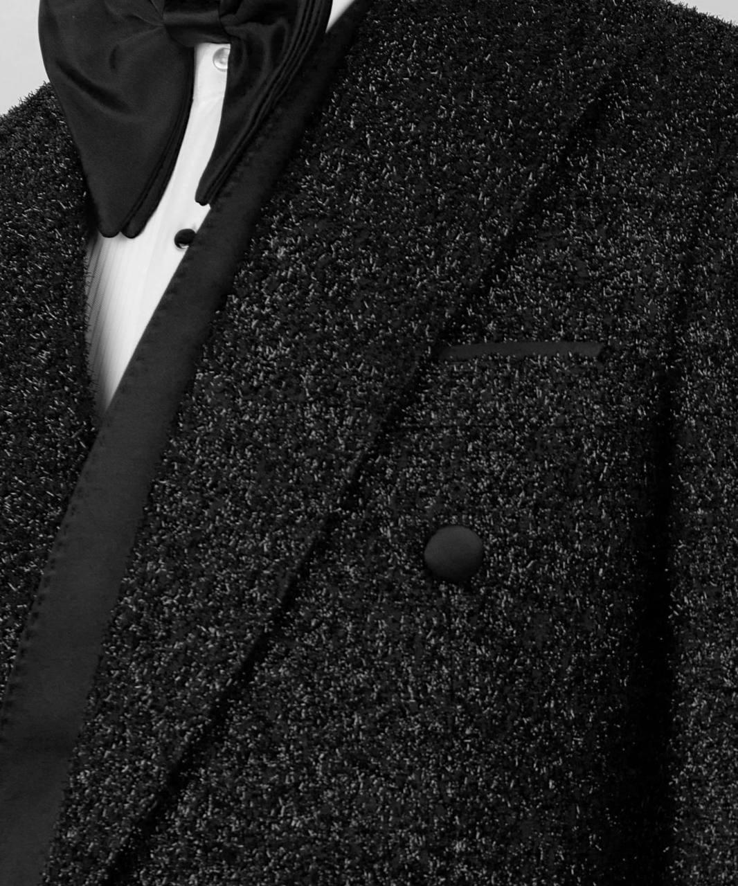 Close-up of a textured black coat with a bow tie and white shirt underneath.