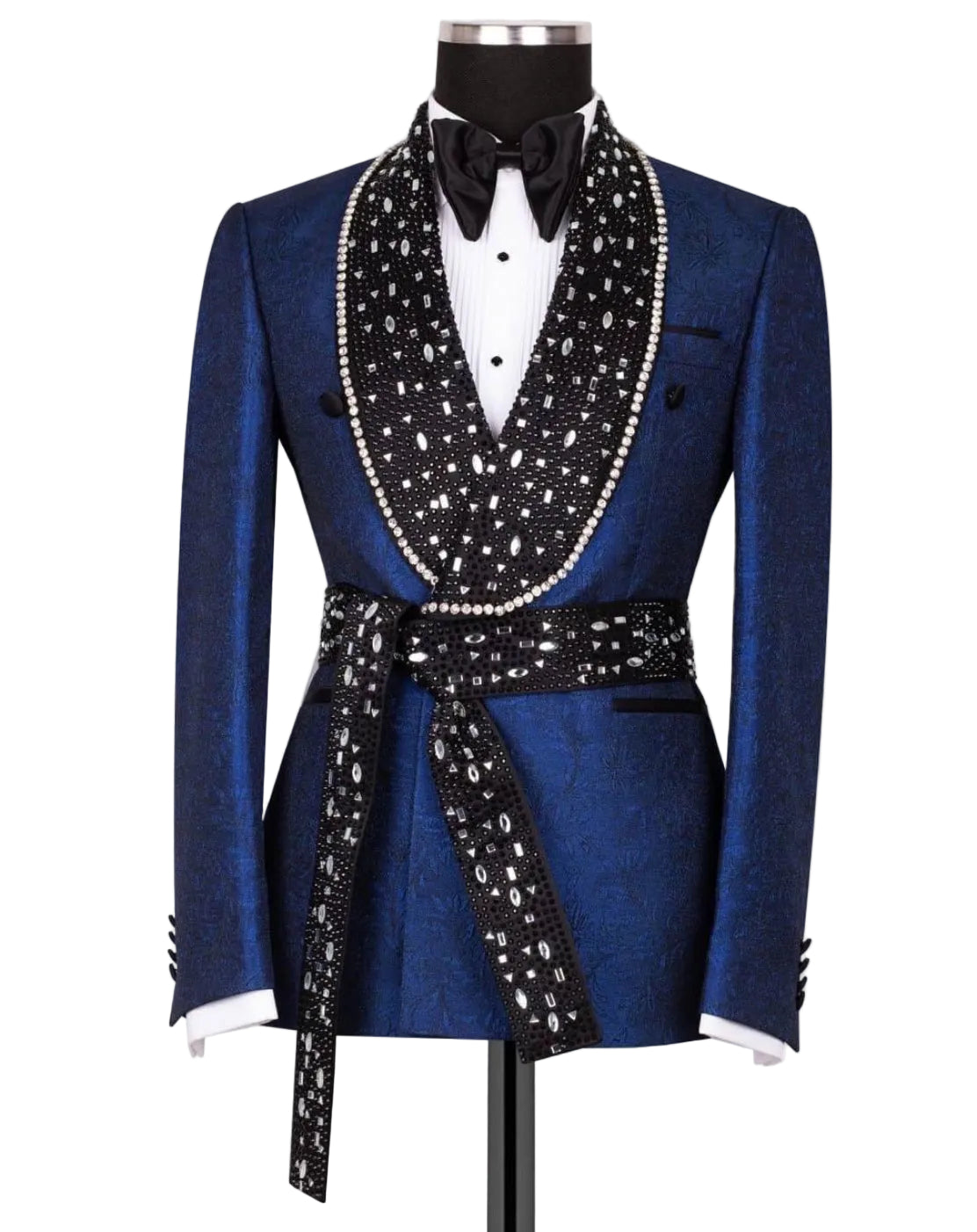 A royal blue textured tuxedo jacket with a black shawl collar heavily embellished with white pearls, a matching black waist tie, a black bow tie, and a white dress shirt, displayed on a mannequin.