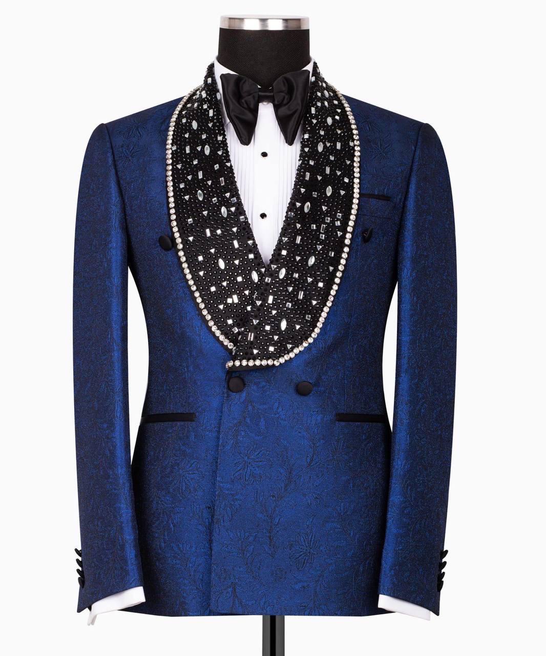 A royal blue patterned tuxedo jacket with a black beaded and pearl-trimmed shawl collar, displayed on a mannequin with a white dress shirt and black bow tie against a white background.