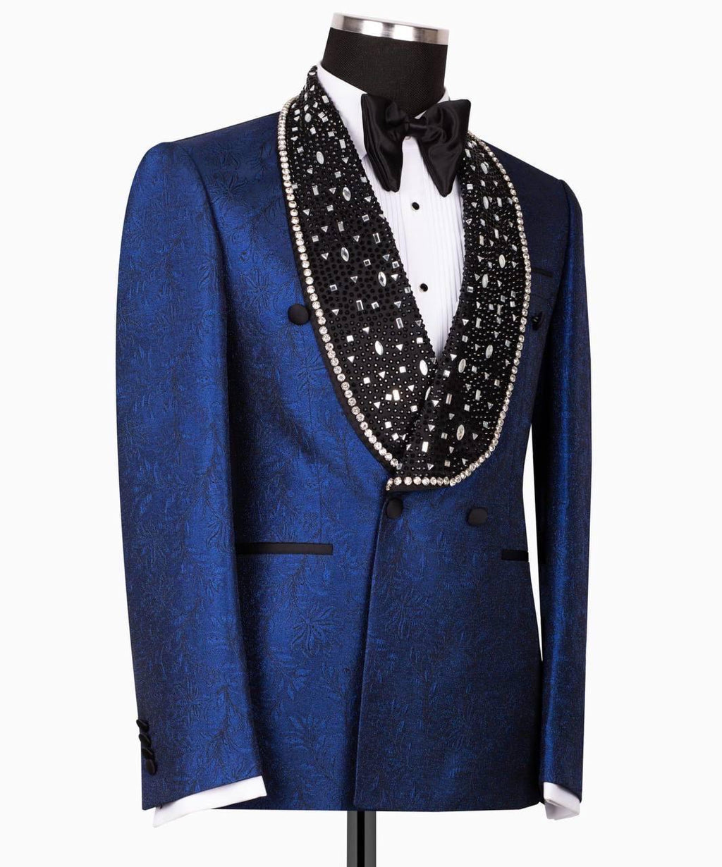 A royal blue patterned tuxedo jacket displayed on a mannequin, featuring a black beaded lapel with a white pearl border, a black bow tie, and a white dress shirt.
