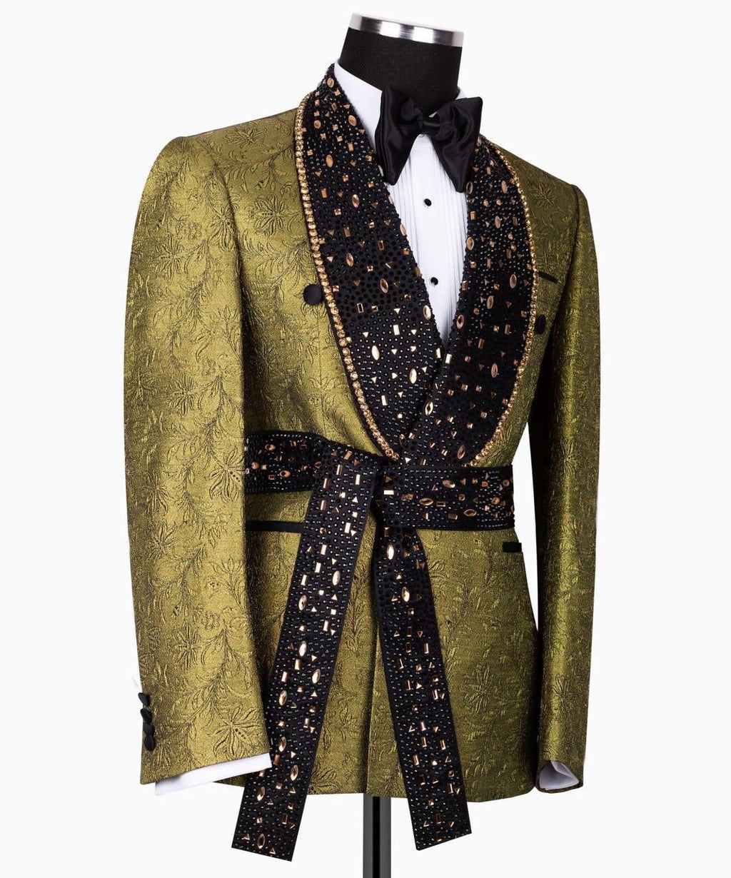 A men's tuxedo jacket displayed on a black mannequin torso, featuring a textured olive green jacquard body with wide black shawl lapels and a matching self-tie waist sash, styled with a white pleated shirt and black bow tie.