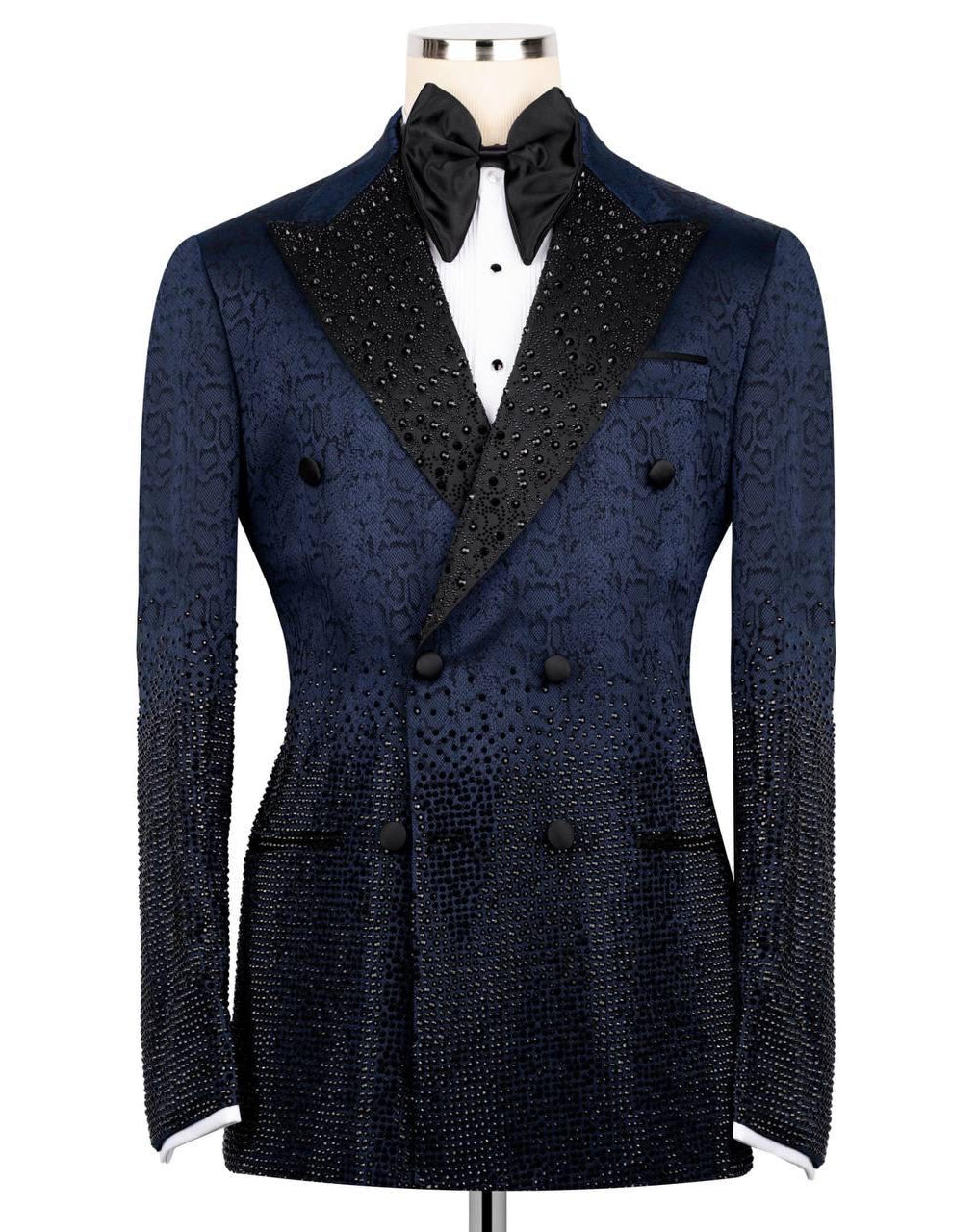 A dark navy blue double-breasted tuxedo jacket with a textured pattern, black satin peak lapels embellished with rhinestones, and a black bow tie, displayed on a mannequin against a white background.