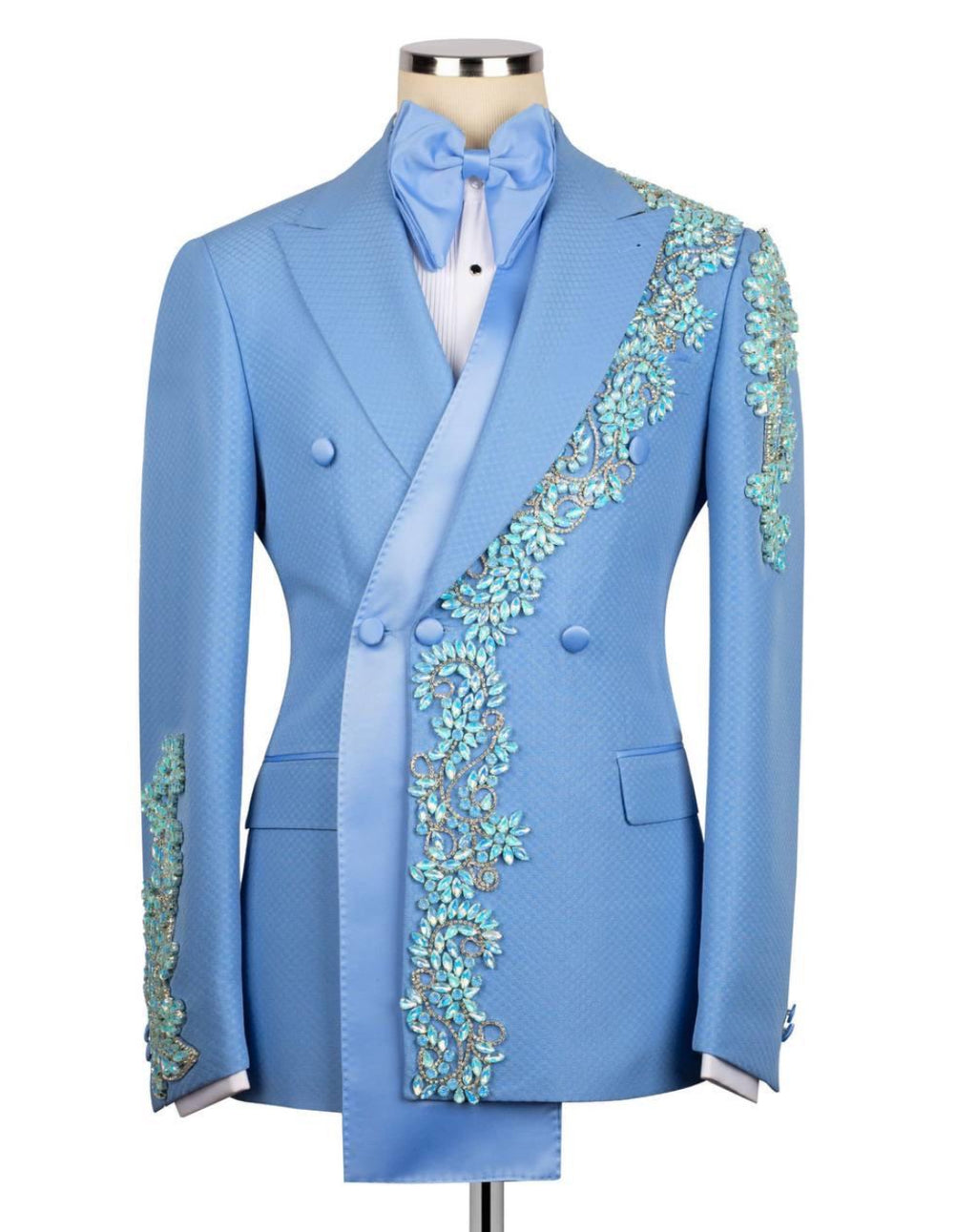 A light blue double-breasted tuxedo jacket with intricate turquoise and gold floral embroidery along the lapels and sleeves, displayed on a mannequin with a matching light blue satin bow tie and white shirt.