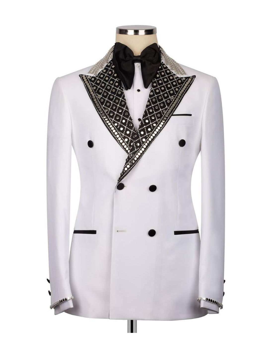 A white double-breasted tuxedo jacket with black lapels heavily embellished with silver rhinestones, displayed on a mannequin with a black bow tie and white shirt.