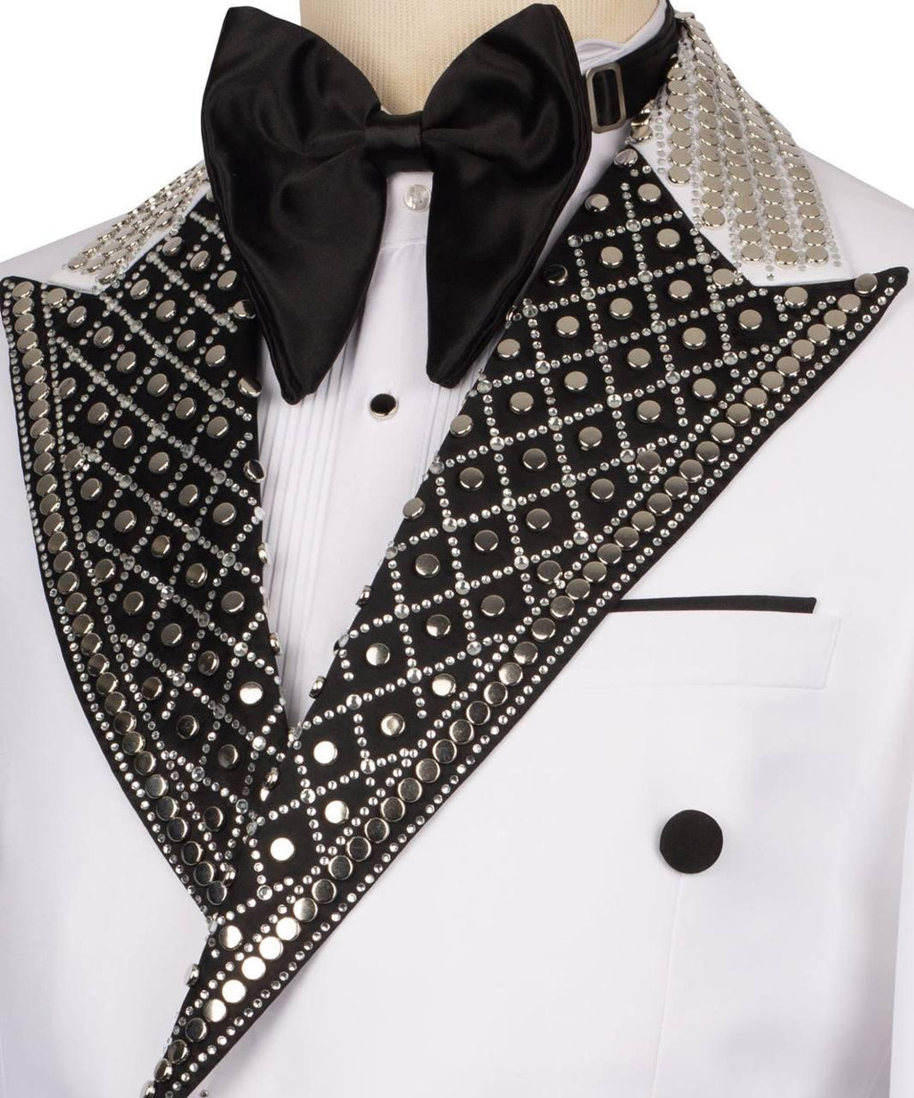 A close-up of a formal tuxedo jacket on a mannequin, featuring a white double-breasted jacket with black satin peak lapels heavily embellished with silver rhinestones and sequins, a black satin bow tie, and a white pleated shirt.