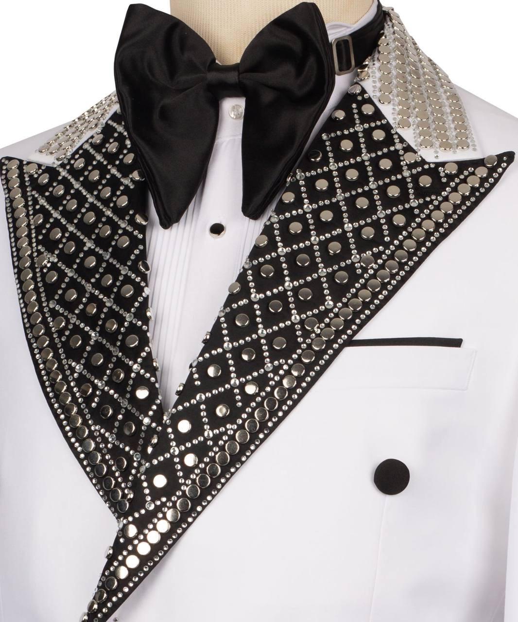 A close-up of a formal tuxedo jacket on a mannequin, featuring a white double-breasted jacket with black satin peak lapels heavily embellished with silver rhinestones and sequins, a black satin bow tie, and a white pleated shirt.