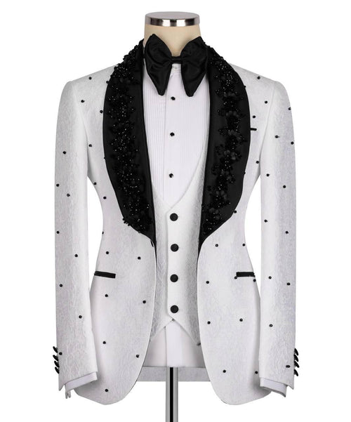 A white tuxedo jacket with black polka dots and black beaded lapels, styled on a mannequin with a white pleated vest, black bow tie, and black satin collar.