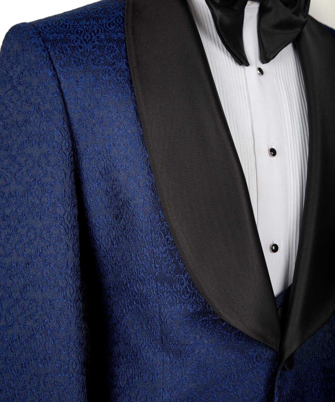 A close-up of a men's formal tuxedo jacket featuring a textured royal blue patterned fabric body with contrasting black satin peak lapels, paired with a white pleated shirt and black bow tie.