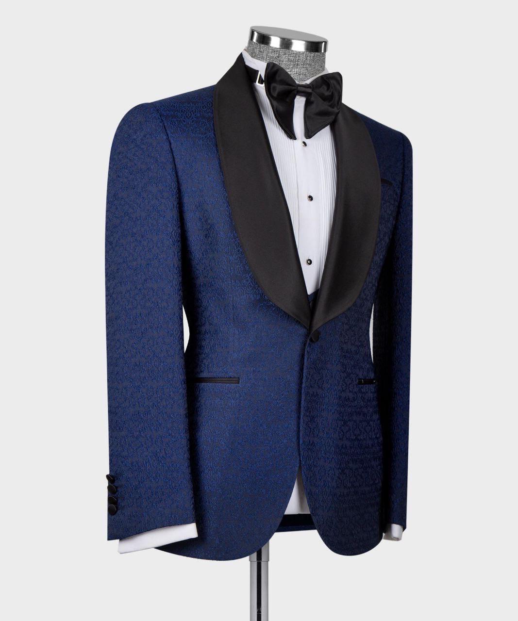 A blue patterned tuxedo jacket with black satin peak lapels, displayed on a mannequin torso with a white dress shirt, black bow tie, and black cufflinks, against a light gray background.