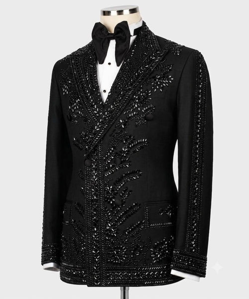 A black double-breasted tuxedo jacket embellished with intricate beadwork and sequins, displayed on a mannequin with a white shirt and black bow tie against a light gray background.