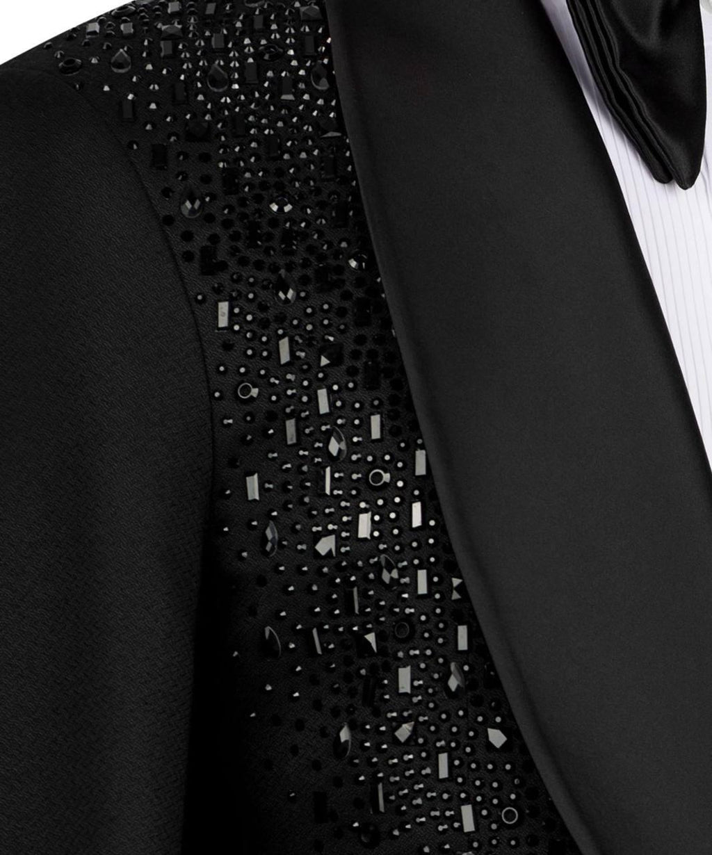 Close-up of a black tuxedo jacket with a heavily embellished beaded and sequined yoke panel, paired with a black satin lapel, white pinstriped shirt, and black bow tie.