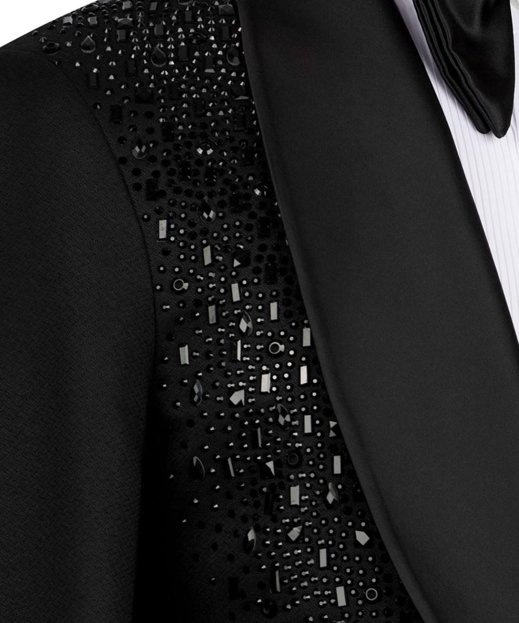 Close-up of a black tuxedo jacket with a heavily embellished beaded and sequined yoke panel, paired with a black satin lapel, white pinstriped shirt, and black bow tie.