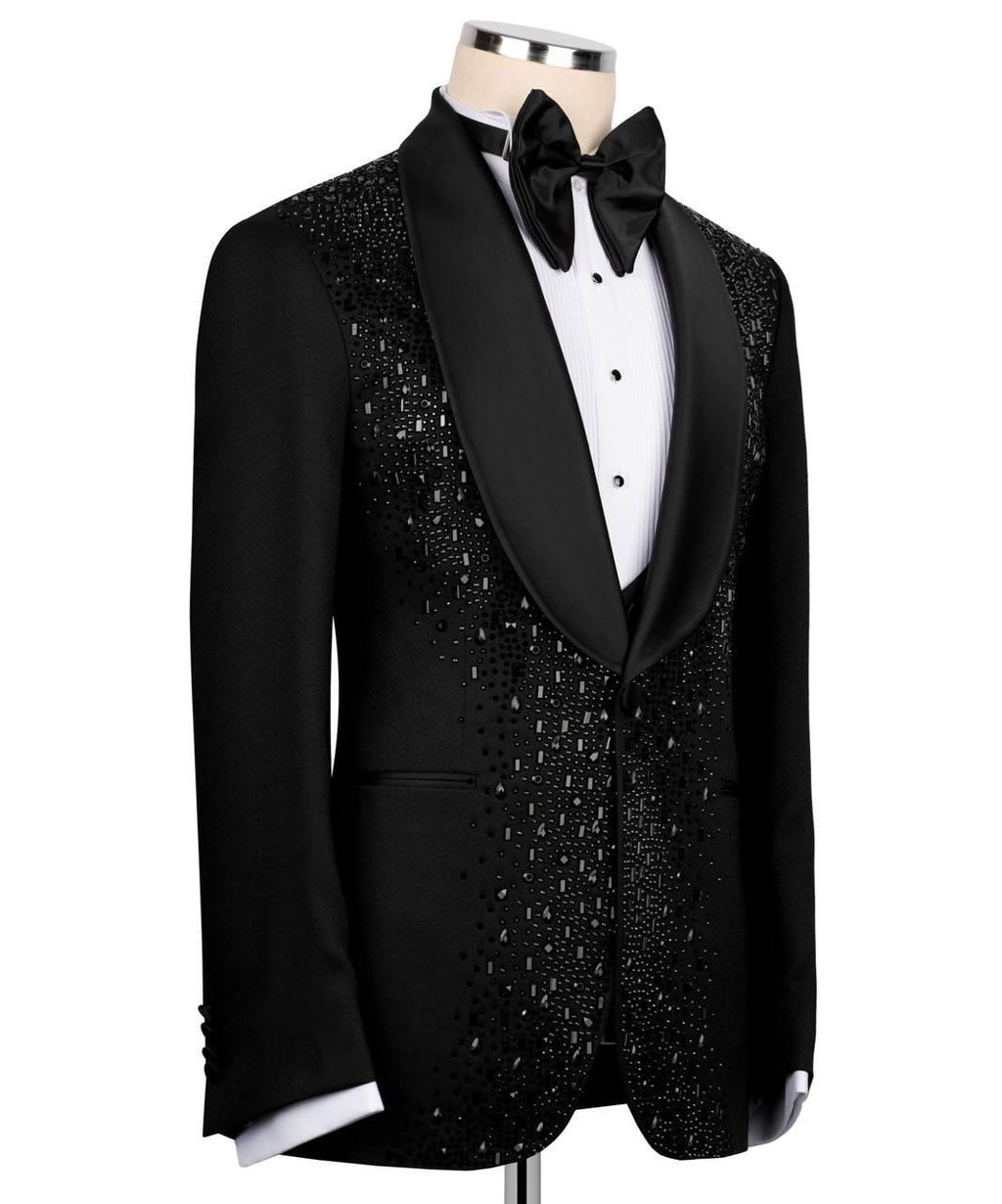 A black tuxedo jacket with a black satin shawl collar and dense silver rhinestone embellishments on the front panel, styled on a mannequin with a white dress shirt and black bow tie against a white background.