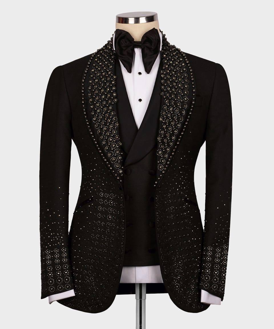 A black formal tuxedo jacket with intricate silver rhinestone embellishments on the shawl collar, lapels, and cuffs, displayed on a mannequin with a black vest, white shirt, and black bow tie.