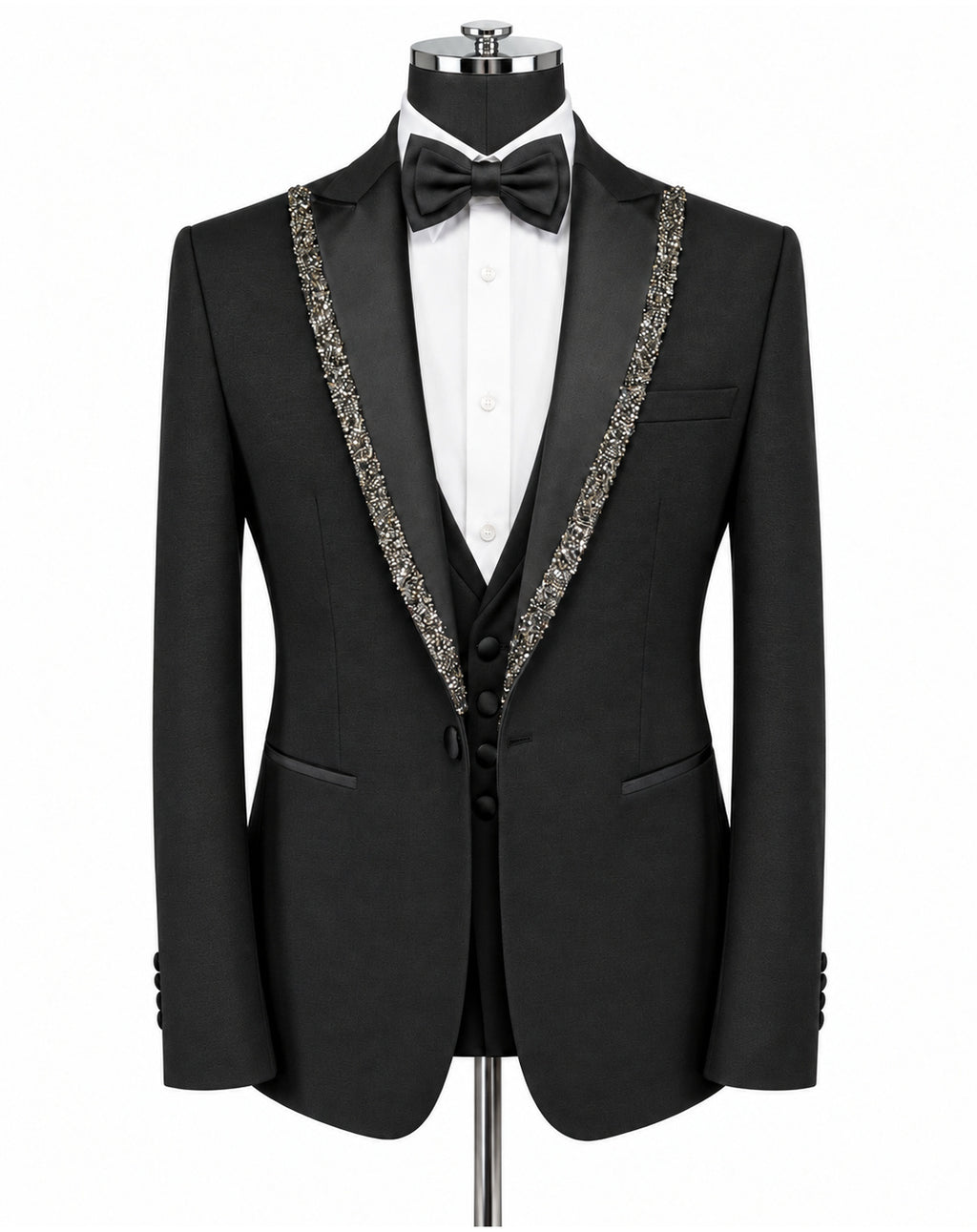 A black tuxedo jacket displayed on a mannequin with a white dress shirt, black bow tie, and matching black vest. The jacket features ornate silver beaded trim along the notched lapels.