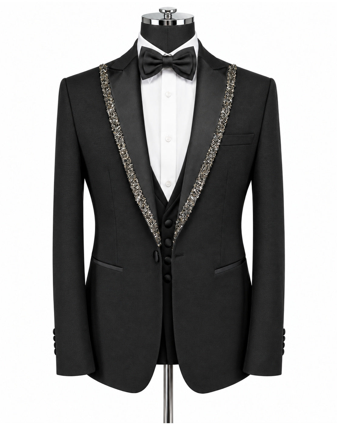 A black tuxedo jacket displayed on a mannequin with a white dress shirt, black bow tie, and matching black vest. The jacket features ornate silver beaded trim along the notched lapels.