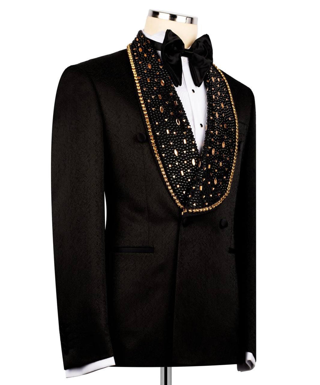 A black tuxedo jacket with a heavily embellished black velvet shawl collar covered in gold and silver rhinestones, styled on a mannequin with a white dress shirt and black bow tie.