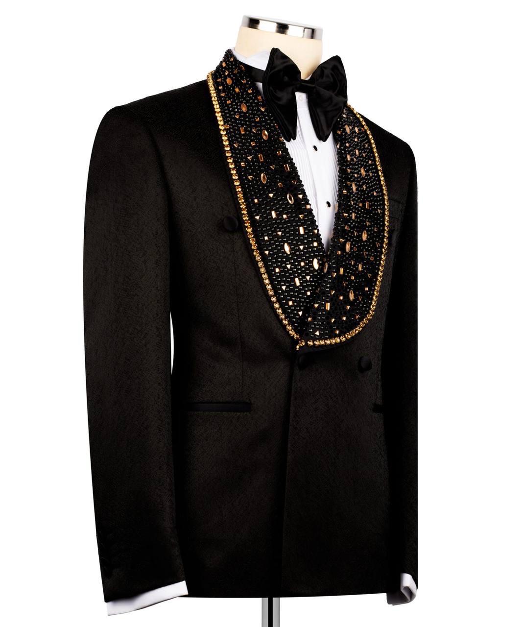 A black tuxedo jacket with a heavily embellished black velvet shawl collar covered in gold and silver rhinestones, styled on a mannequin with a white dress shirt and black bow tie.